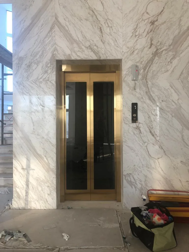 Gold-tone elevator entrance set within veined wall cladding